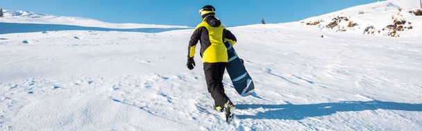 plan panoramique d'un sportif tenant du snowboard alors qu'il marchait sur la neige
  - Photo, image