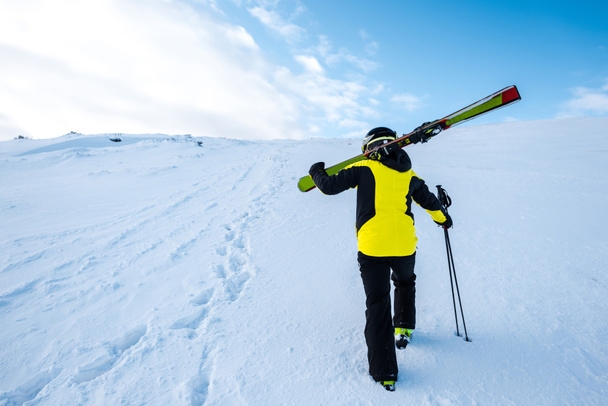 πίσω όψη του σκιέρ περπάτημα με μπαστούνια του σκι στο χιόνι  - Φωτογραφία, εικόνα