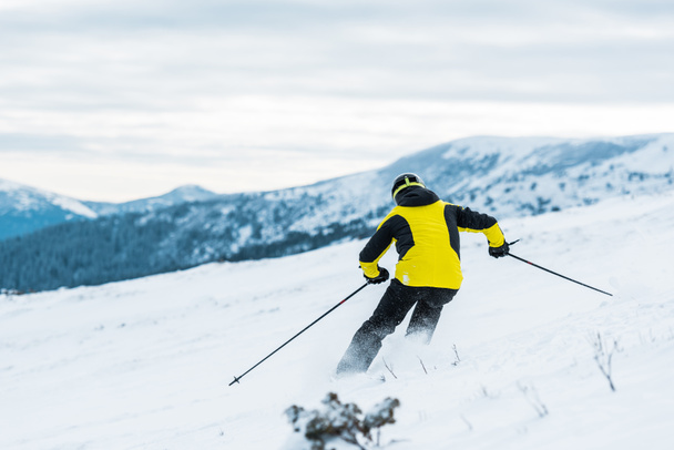 back view of skier in helmet holding sticks and skiing on slope in wintertime  - Photo, Image