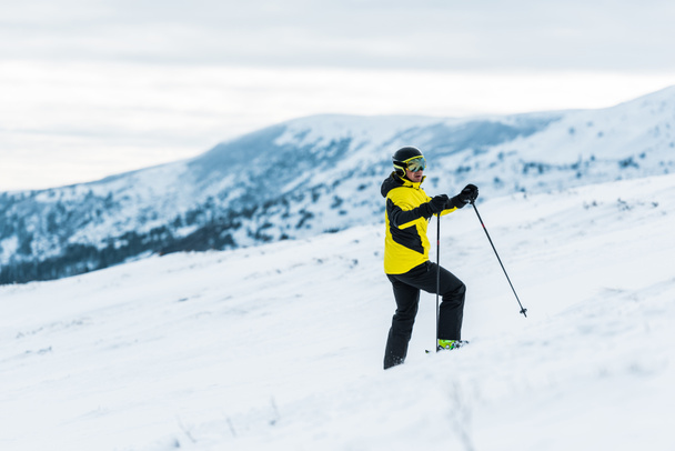 esquiador en casco sosteniendo palos y de pie en la pendiente en invierno
  - Foto, Imagen