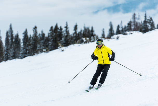 σκιέρ σε κράνος κρατώντας μπαστούνια και σκι στην πλαγιά στα βουνά  - Φωτογραφία, εικόνα