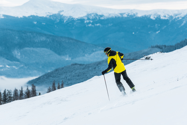 back view of skier holding sticks and skiing on slope with snow in mountains  - Photo, Image