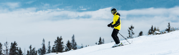 panoramic shot of sportsman in helmet skiing on slope near mountains  - Photo, Image