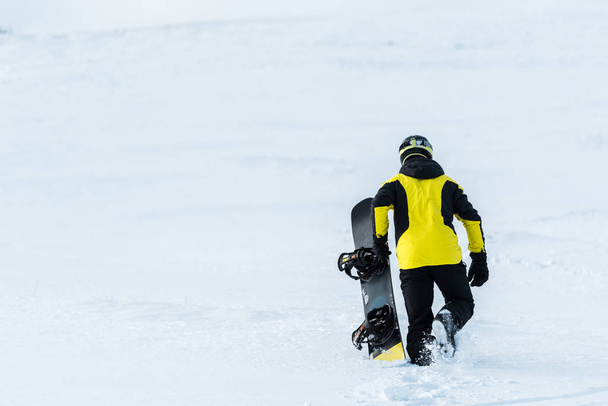 takaisin näkymä urheilija tilalla lumilauta kävellessään lumella
  - Valokuva, kuva