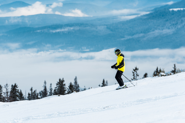 σκιέρ σε κράνος κρατώντας μπαστούνια και σκι στην πλαγιά το χειμώνα  - Φωτογραφία, εικόνα