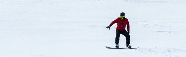 Panoramaaufnahme eines Snowboarders mit Helm, der auf einem Hang mit weißem Schnee unterwegs ist  - Foto, Bild