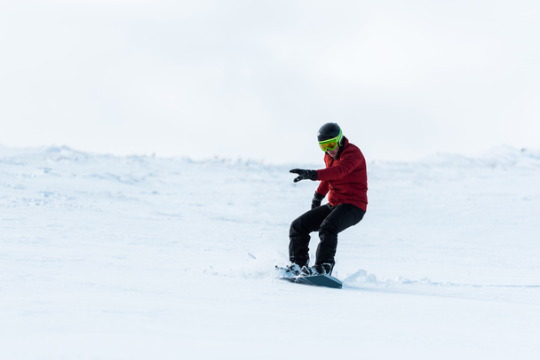 atletische snowboarder in helm rijden op helling buiten  - Foto, afbeelding