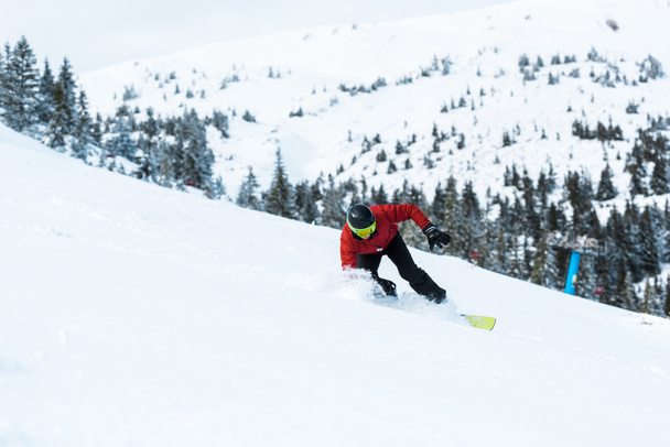山の近くの斜面に乗ってヘルメットをかぶって運動するスノーボーダー  - 写真・画像