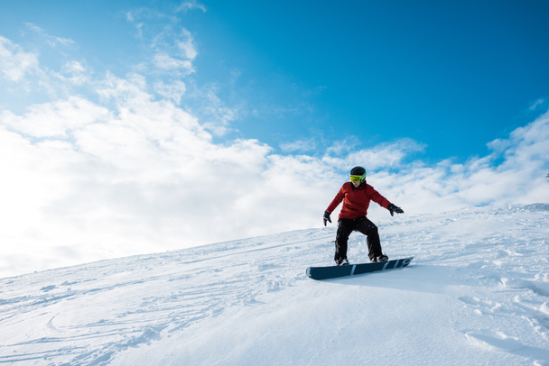 snowboarder atletico in casco cavalcando sul pendio contro il cielo blu con nuvole
  - Foto, immagini