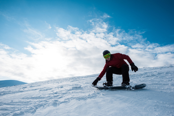athletic snowboarder in helmet riding on slope against blue sky  - Foto, imagen