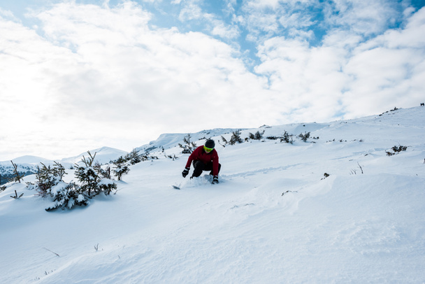 lumilautailija suojalaseissa ja kypärä ratsastus rinteessä vuorilla vastaan sininen taivas
  - Valokuva, kuva