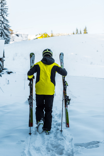 achteraanzicht van skiër in helm met skisticks tijdens het wandelen op sneeuw in de winter  - Foto, afbeelding