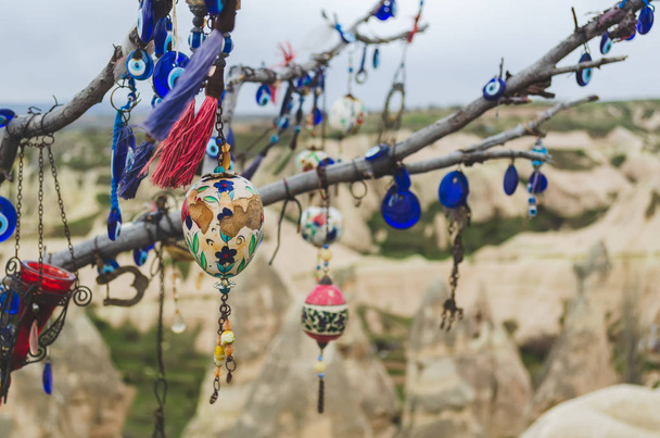 Traditionelle türkische Amulette und Dekorationen hängen an den Zweigen eines Wunschbaums vor dem Hintergrund der Vulkanlandschaft Kappadokiens - Foto, Bild