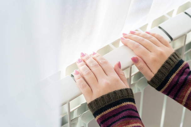 Meisje warmt de bevroren handen boven hete radiator, van dichtbij bekijken - Foto, afbeelding