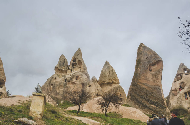 Dwellings in the rocks of volcanic tuff in Cappadocia. A group of tourists visiting the sights of the National Park of Goreme - Fotoğraf, Görsel