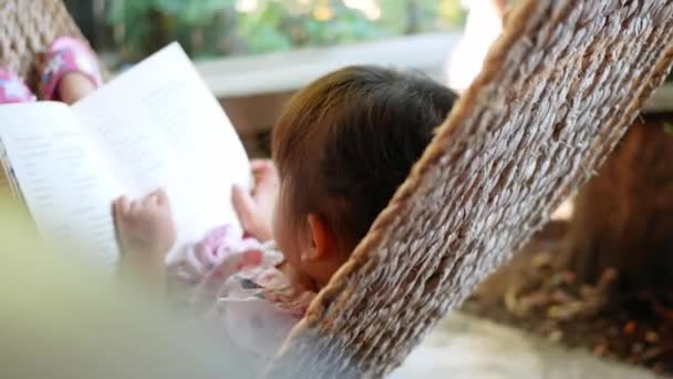 Linda niña que relaja y lee un libro tumbado en la hamaca al aire libre en el jardín
. - Metraje, vídeo