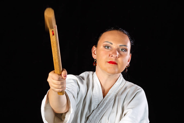 A young brunette woman in a white kimono is engaged with nunchucks on a black background. - Foto, afbeelding