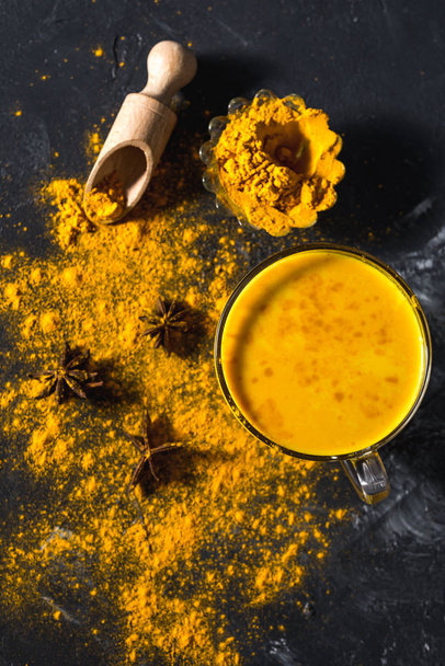 Golden turmeric milk on the dark background with spices cinnamon and ingredients - Fotó, kép