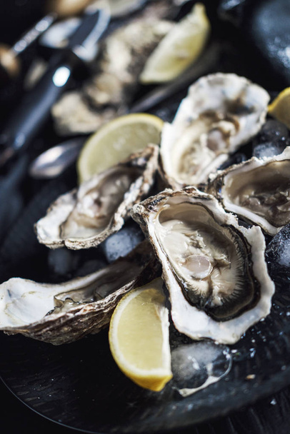 Open oysters with lemon in a black plate - 写真・画像