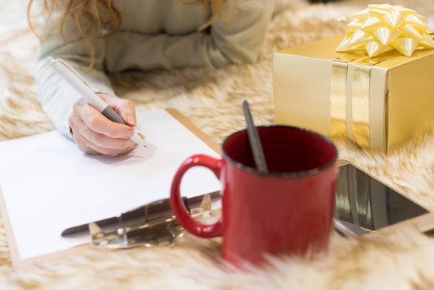 zbliżenie kobieta ręka pisanie z pudełko prezent i telefon komórkowy na dywan w domu - Zdjęcie, obraz