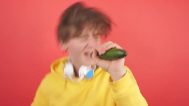 A young man in a sweatshirt sings in a cucumber on a red background. - Metraje, vídeo