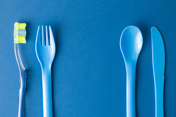 Kunststof vork, lepel en mes met tandenborstel op blauwe achtergrond maaltijd en mondhygiëne abstract. - Foto, afbeelding