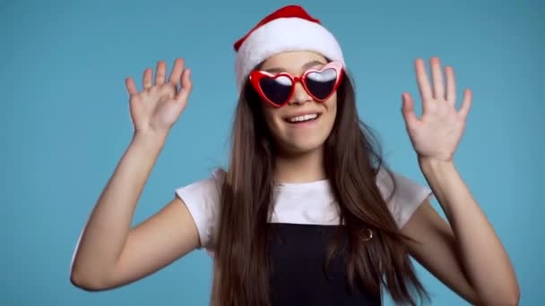 Dancing girl with Santa hat having fun, rejoices isolated over blue studio background. Concept of Christmas, New Year, happiness, party, winning. - Footage, Video