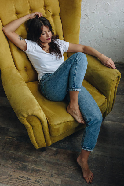 Beautiful young woman sitting in yellow armchair - Foto, afbeelding