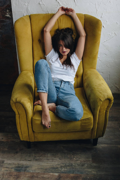 Beautiful young woman sitting in yellow armchair - Fotó, kép