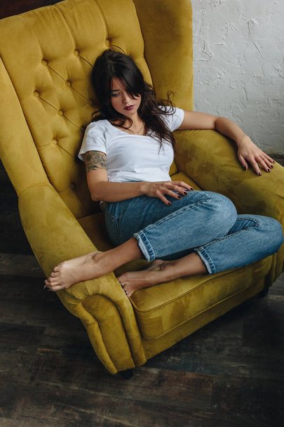 Beautiful young woman sitting in yellow armchair - Foto, Bild