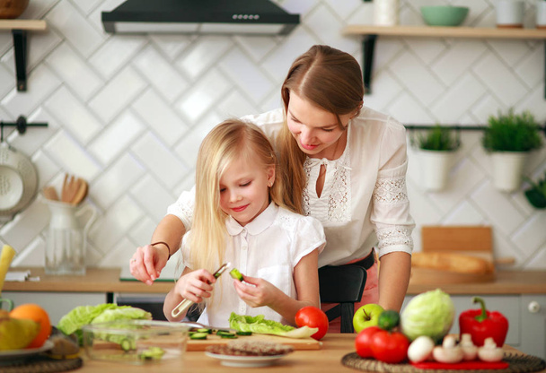 Mother teaches her child daughter how to cook in kitchen - Foto, afbeelding