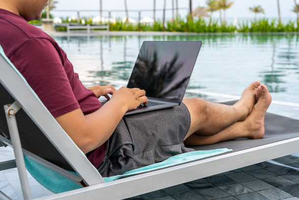 Homme utilisant un ordinateur portable tout en étant assis sur une chaise à la piscine
 - Photo, image