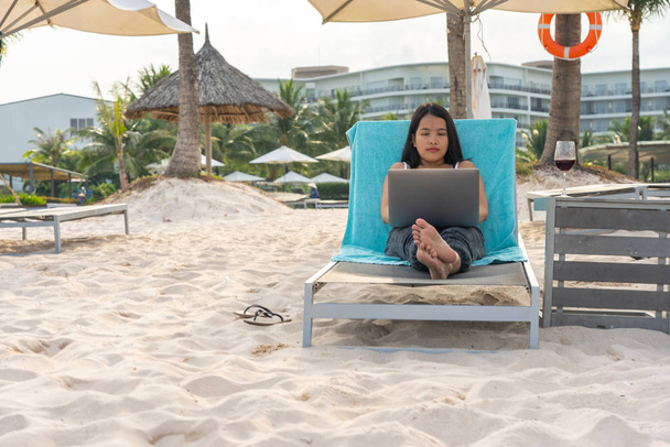 Giovane donna che utilizza il computer portatile mentre si rilassa sulla spiaggia
 - Foto, immagini