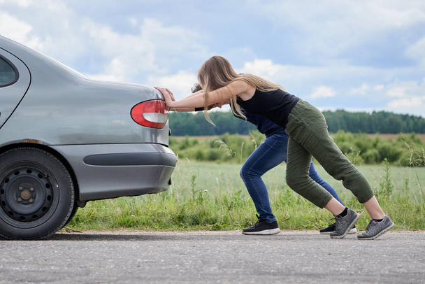 Kaksi tyttöä työntää autonsa, joka on loppunut bensiinin pitkin Country Road
 - Valokuva, kuva