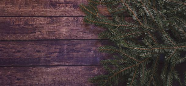 A dark green spruce branch lies on left by the dark brown wooden table. A festive Christmas mood in dark colors with space for text banner - Photo, Image
