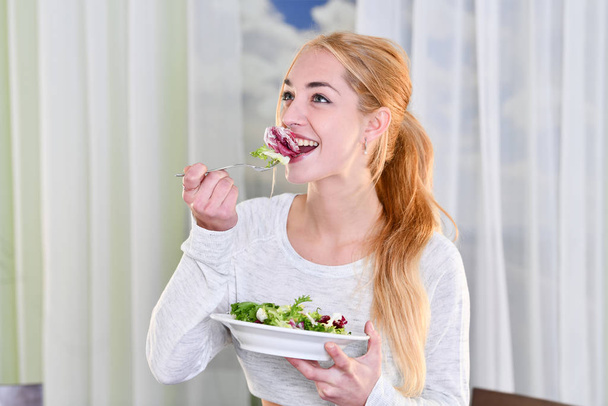 Kobieta uśmiecha się jedząc zdrową sałatkę - Zdjęcie, obraz