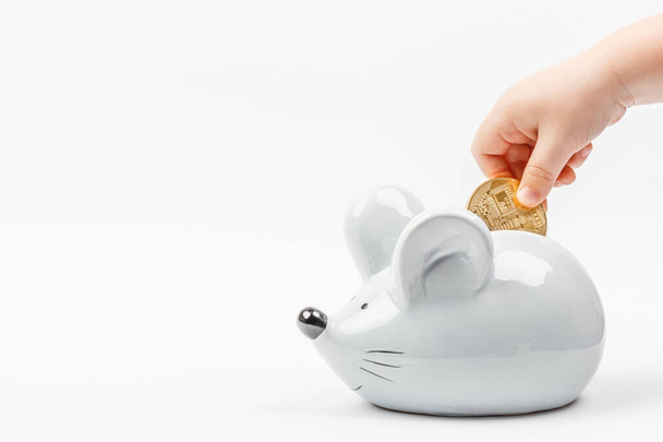 Το χέρι του μικρού παιδιού βάζει ένα bitcoin σε ένα γκρι ποντίκι ή κουμπαρά αρουραίου σε ένα λευκό φόντο με θέση για κείμενο. - Φωτογραφία, εικόνα