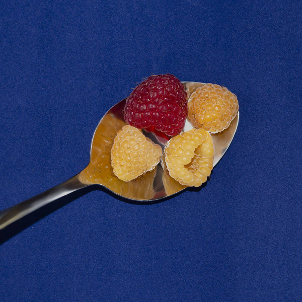 Ripe raspberries in a spoon. On a blue background - Photo, Image