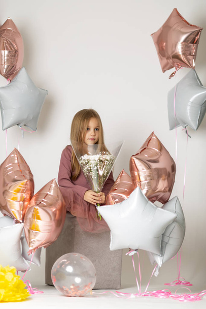 seven year old girl sitting on a white background dress with a bouquet of white wildflowers and balloons - 写真・画像