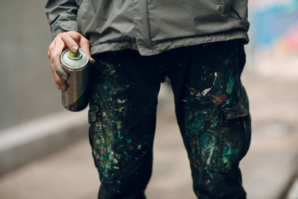 Graffiti artist in clothes stained with paint spray can in hand - 写真・画像