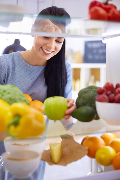 Mujer sonriente sacando una fruta fresca de la nevera, concepto de comida saludable - Foto, Imagen