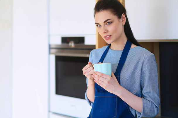 Portrait of young woman with cup against kitchen interior background - Photo, Image