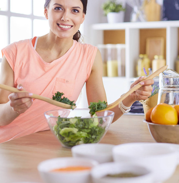 Smiling young woman mixing fresh salad in the kitchen. - Photo, Image