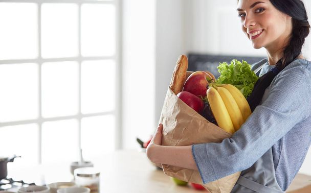 Young woman holding grocery shopping bag with vegetables .Standing in the kitchen - Φωτογραφία, εικόνα