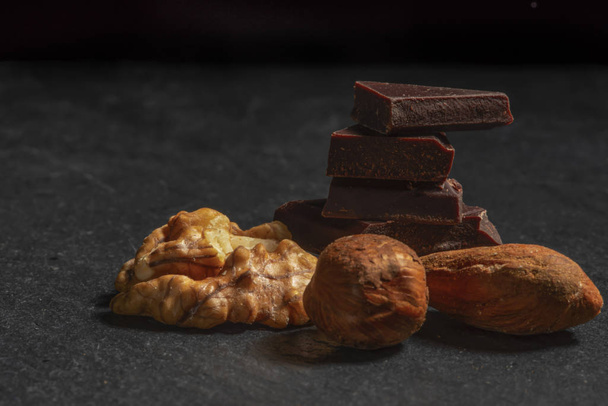 Dark chocolate in nuts on a stone. Dark background. - Foto, Bild