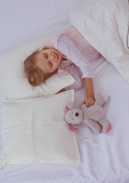 Lapsi pieni tyttö nukkuu sängyssä lelu nallekarhu
. - Valokuva, kuva
