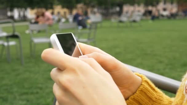 meisje handen met gele mouwen houden witte smartphone in park - Video