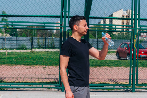 Портрет молодого спортсмена, пьющего воду на баскетбольной площадке
 - Фото, изображение