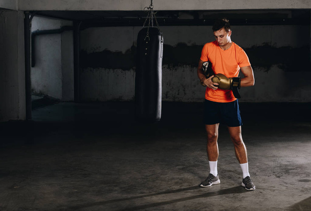 Odhodlaný mladý Muay thajský bojovník v boxerských rukavicích trénink thajský box s boxovací pytel - Fotografie, Obrázek