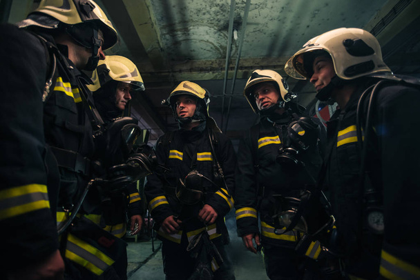 Team of firefighters standing inside ( indoors ) a buliding next to a fire engine. - Foto, imagen